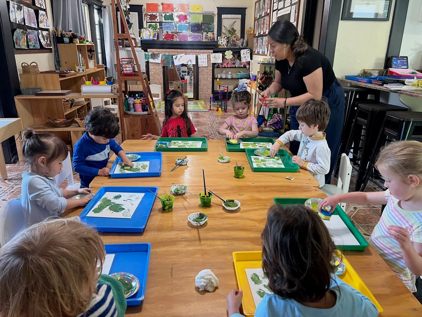 Children sponge-painting together at the table with their teacher